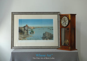 A framed narrative art print, resting on a table, showing a man on the Irish Coast, skimming a stone into the rippling water.