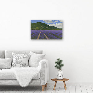 Canvas picture printed from an oil painting of lavender fields. The Art print hangs on a white wall above a table & chair.