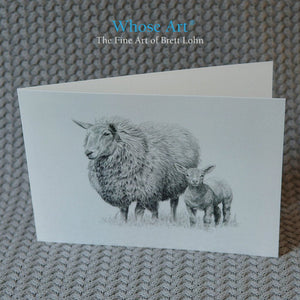 Sheep greeting card standing on a table. The greeting card shows a drawing of a protective sheep & a spring lamb together