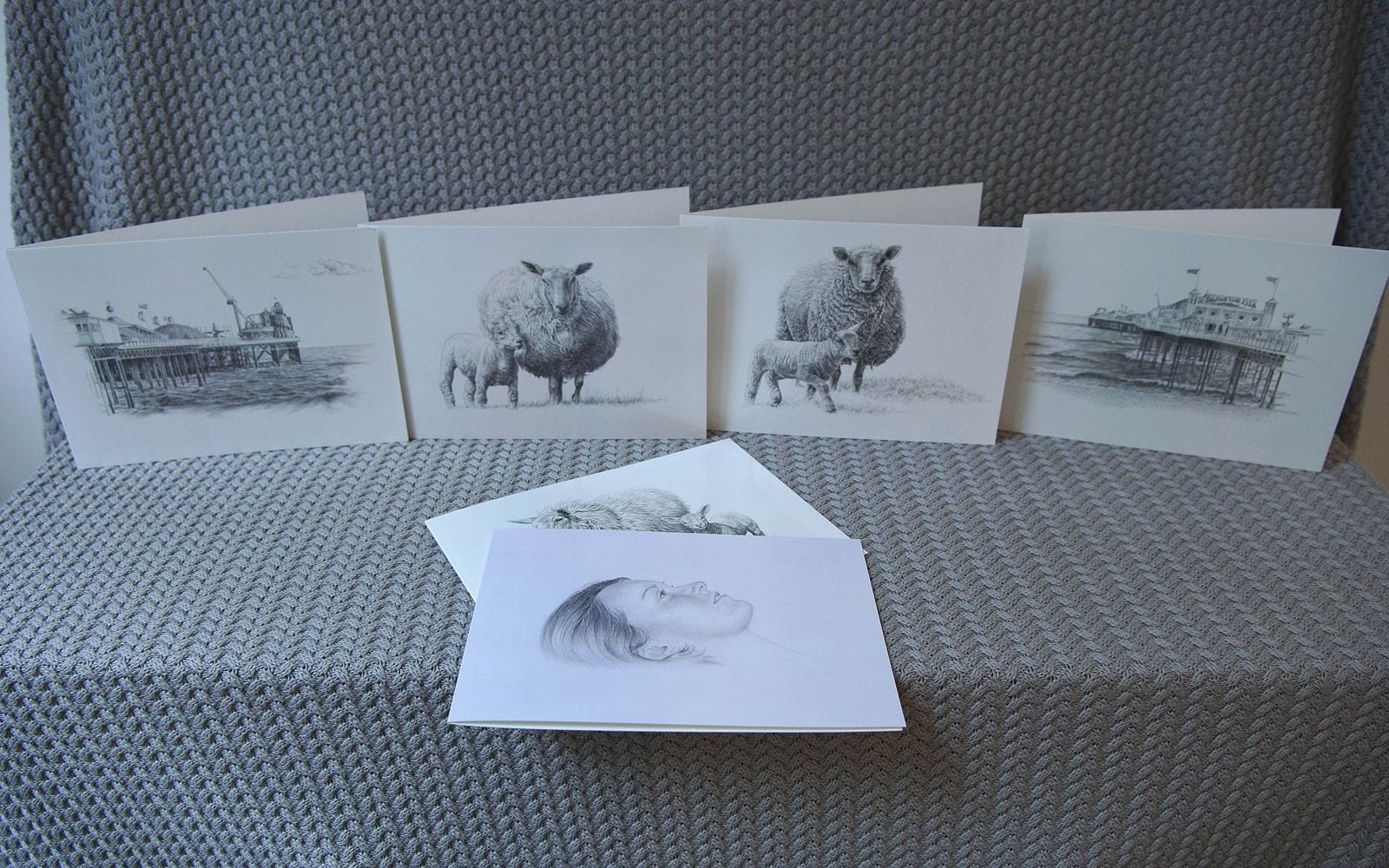 black & white art greeting cards arranged on a table. Some of the art greeting cards feature pencil drawings of sheep, lambs and seascapes.