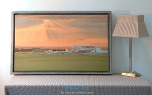 Canvas wall art of a dramatic sunset over Epsom Downs racecourse. The Canvas art print is framed silver and rests on a table.