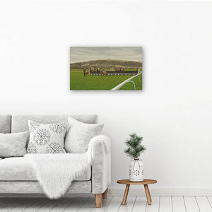 Canvas wall art print of a horse racing painting. The horse art print hangs on a white wall above an armchair and table.