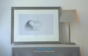 Framed black & white wall art picture of a drawing of a girl's face as she lies daydreaming. Drawn in pencil & framed silver.