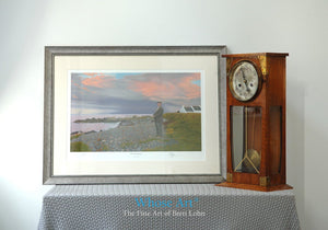 Framed mystic art print of a dusk scene showing a painting of a man holding a heavy stone on a beach by a gathering storm.