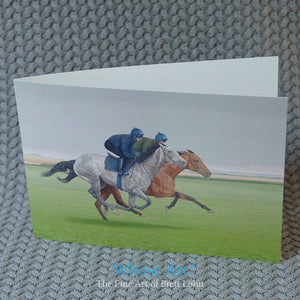 Galloping horse art greeting card on a table. The picture on the greeting card is of two racehorses galloping in training