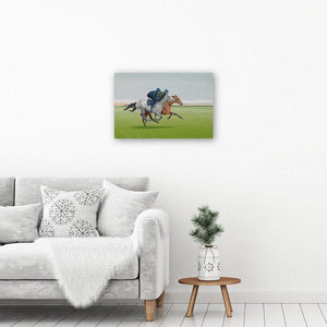 Canvas wall art print of a painting of galloping horses. Picture hangs on a wall above an armchair.