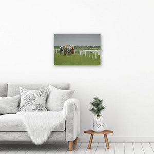 Horse racing art canvas print of a painting of racehorses running under a dramatic grey sky. The canvas print hangs on a wall