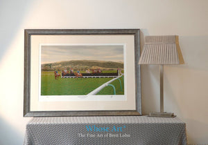 A framed horse racing print showing a painting of racing at Cheltenham Racecourse, framed in silver in an interior decor room