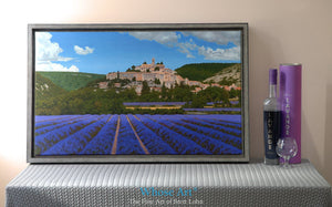 Canvas art print featuring a painting of a village nestling in a Lavender field in Provence, France. The print is framed.