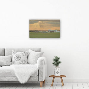A beautiful sunset painting reproduced in a canvas art print hangs on a white wall above a coffee table by a chair.